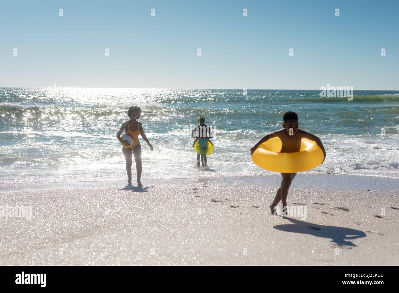 Famiglia afroamericana godendo di vacanze estive insieme in spiaggia contro il cielo limpido in giorno di sole Foto Stock