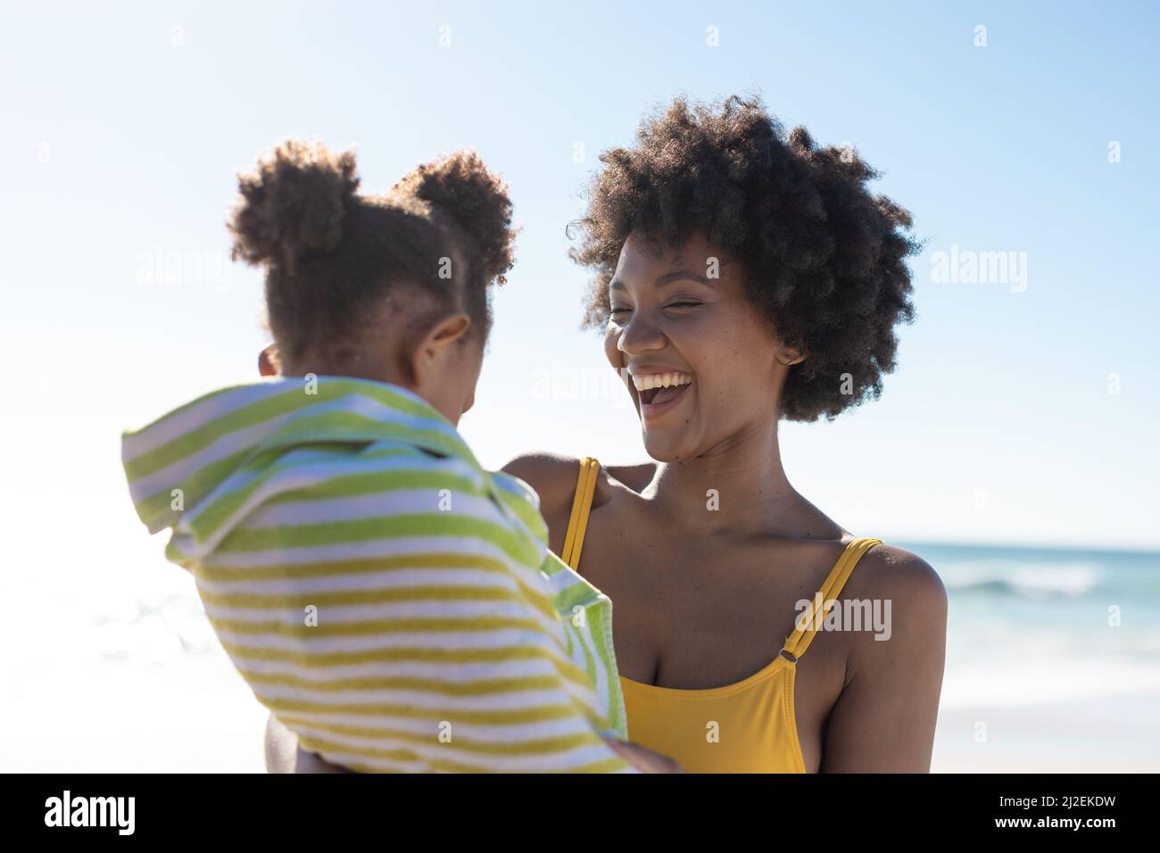 Allegra madre afroamericana con figlia avvolta in asciugamano in spiaggia il giorno di sole Foto Stock