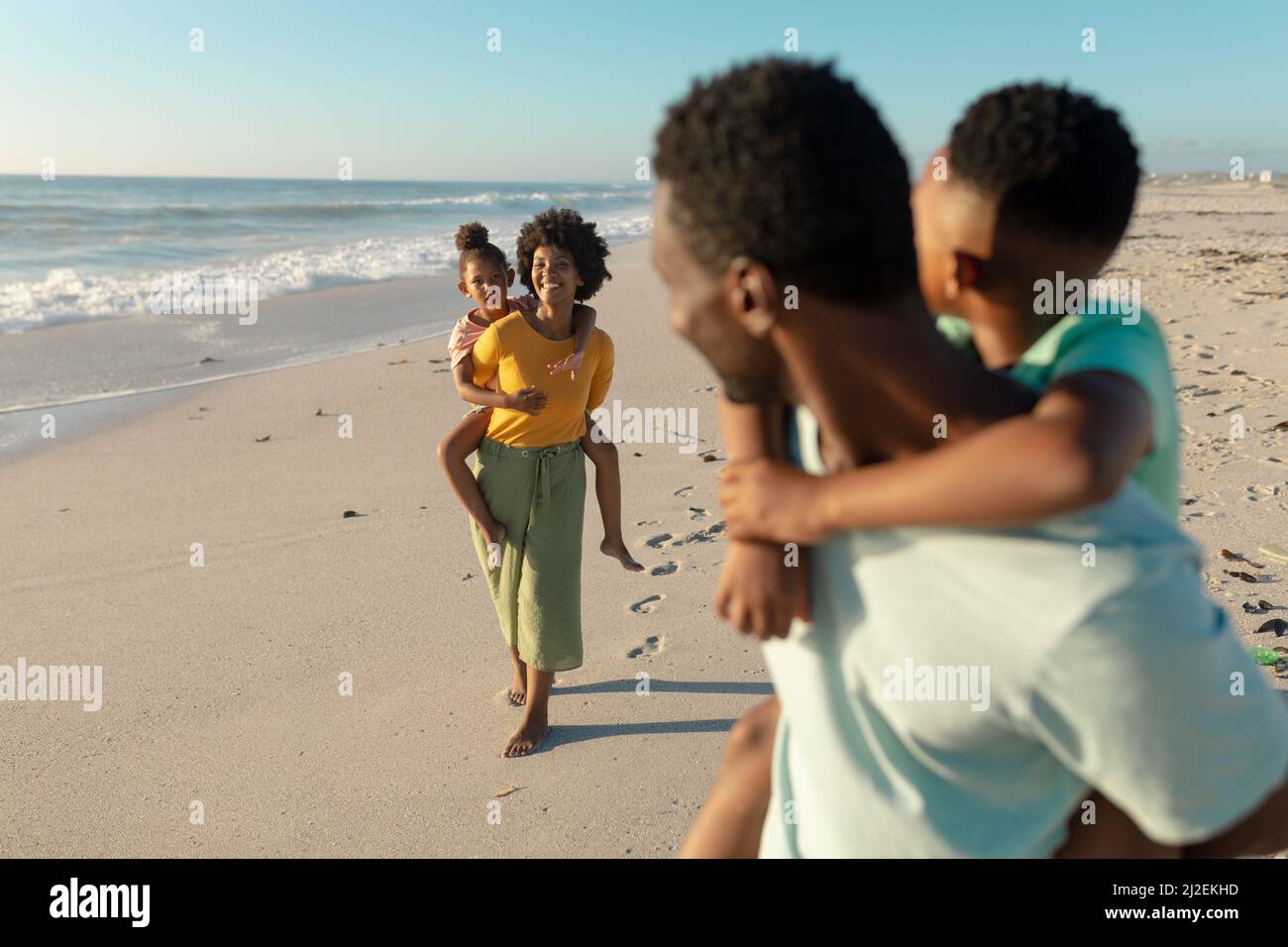Madre afroamericana figlia piggybacking mentre padre e figlio li guardano Foto Stock