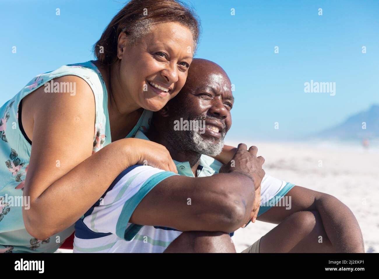 Felice afroamericana anziana che abbraccia uomo in pensione da dietro a spiaggia Foto Stock Felice afroamericana anziana che abbraccia uomo in pensione da dietro a spiaggia Foto Stock