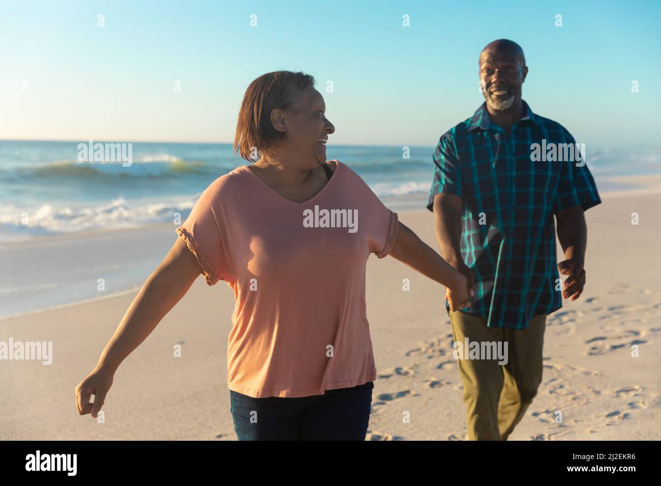 Sorridente anziana afroamericana che tiene una mano di uomo che cammina in spiaggia Foto Stock