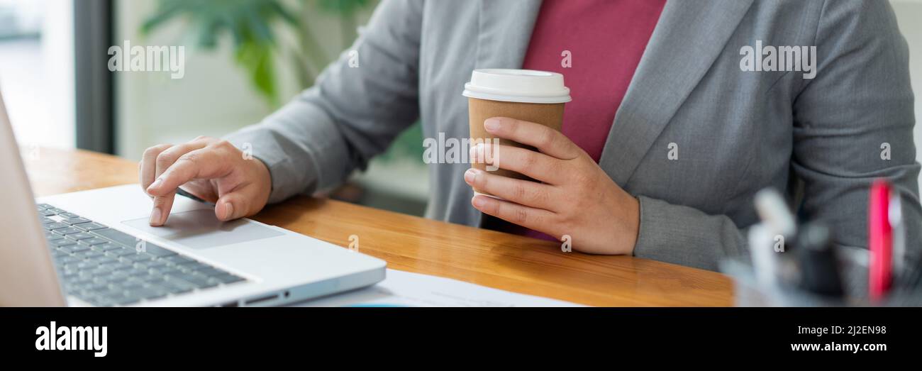 Business analista concetto l'ufficiale femminile che tiene una tazza di caffè digitando informazioni sul computer portatile. Foto Stock
