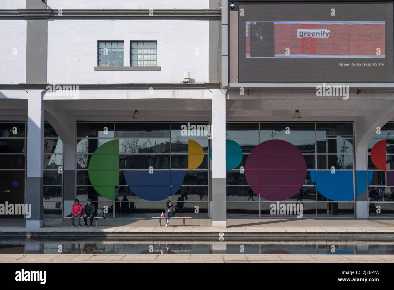La gente si siede all'ombra di Millennium Square in una giornata di sole a Bristol, Regno Unito. Foto Stock