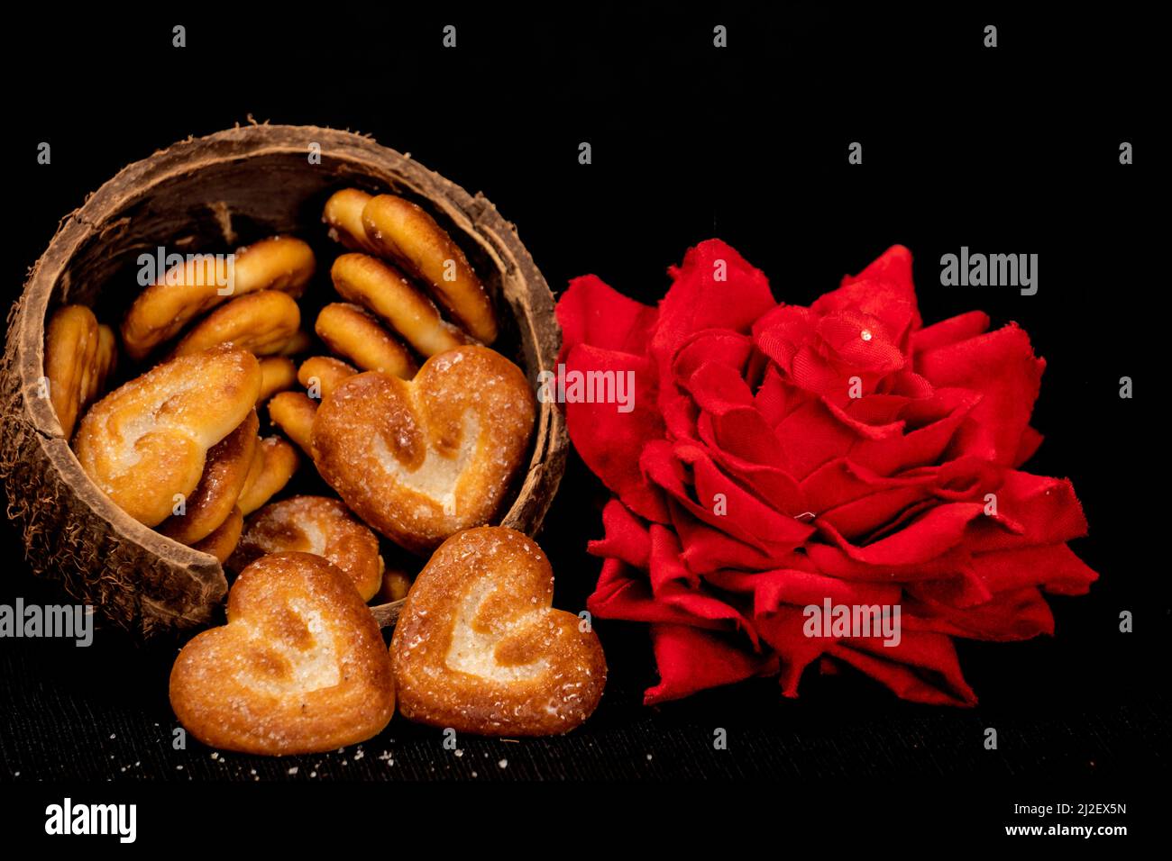 Biscotti a forma di cuore in conchiglia di cocco con rosa rossa, isolato con sfondo nero Foto Stock