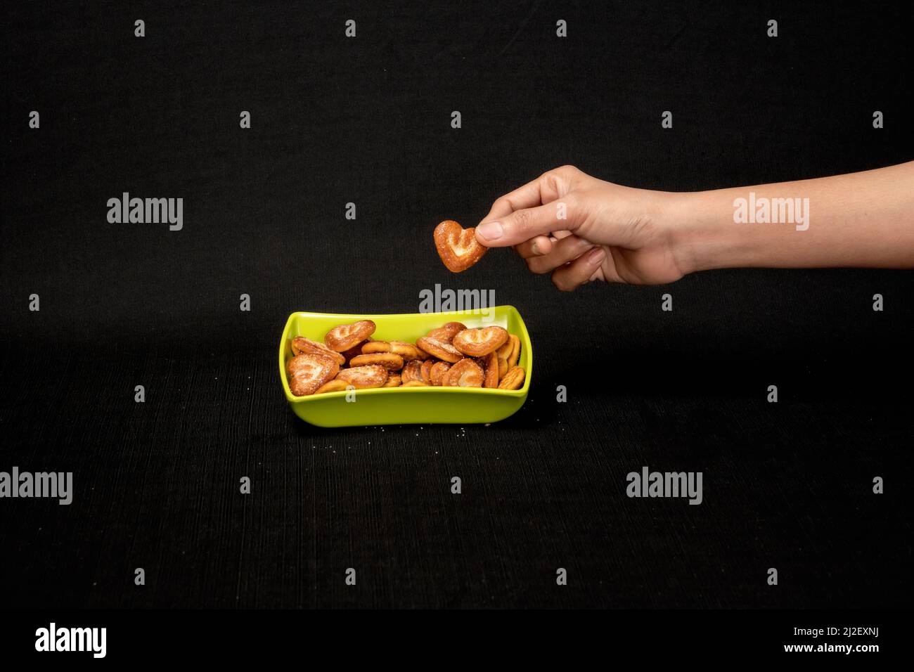 Cuori a forma di biscotto in Green Square Bowl, Boy Hand Pickup the Biscuit, isolato su sfondo nero Foto Stock