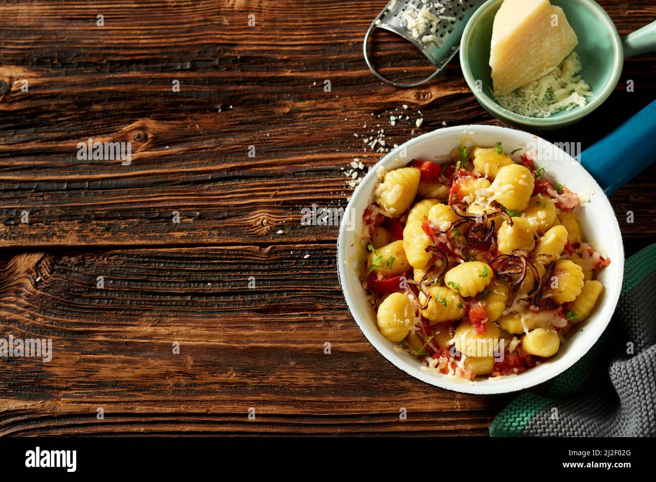 Vista dall'alto della padella con gustosi gnocchi di patate serviti con formaggio grattugiato e pomodori su un tavolo di legno per il pranzo Foto Stock