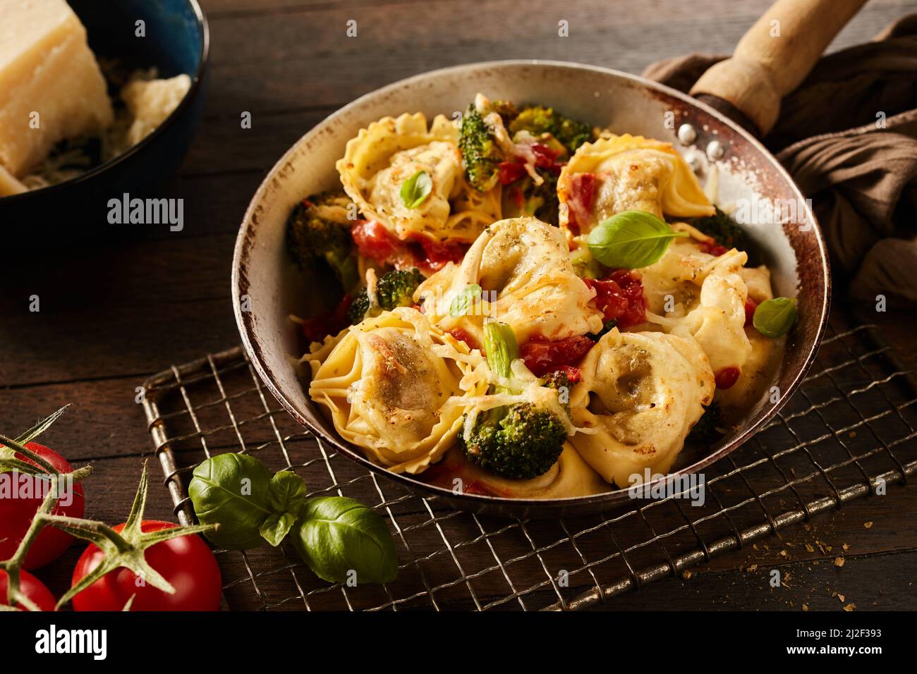 L'appetitosa tortelloni fatta in casa con broccoli e pomodori sul grill in metallo vicino al formaggio in una ciotola su tavola di legno Foto Stock