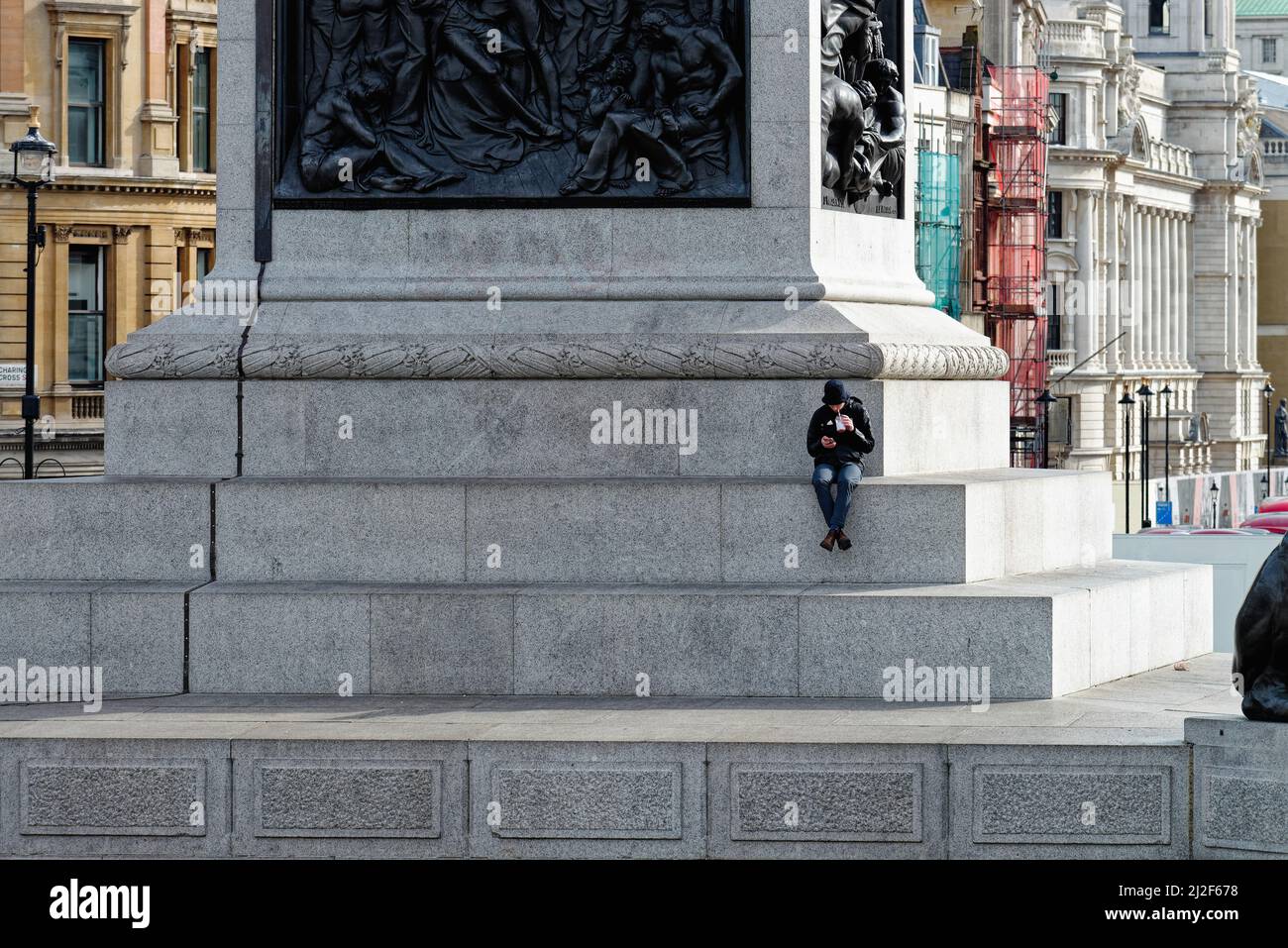 Un maschio soluto seduto sul plinth della colonna di Nelsons usando un telefono mobile Trafalgar Square Central London England UK Foto Stock