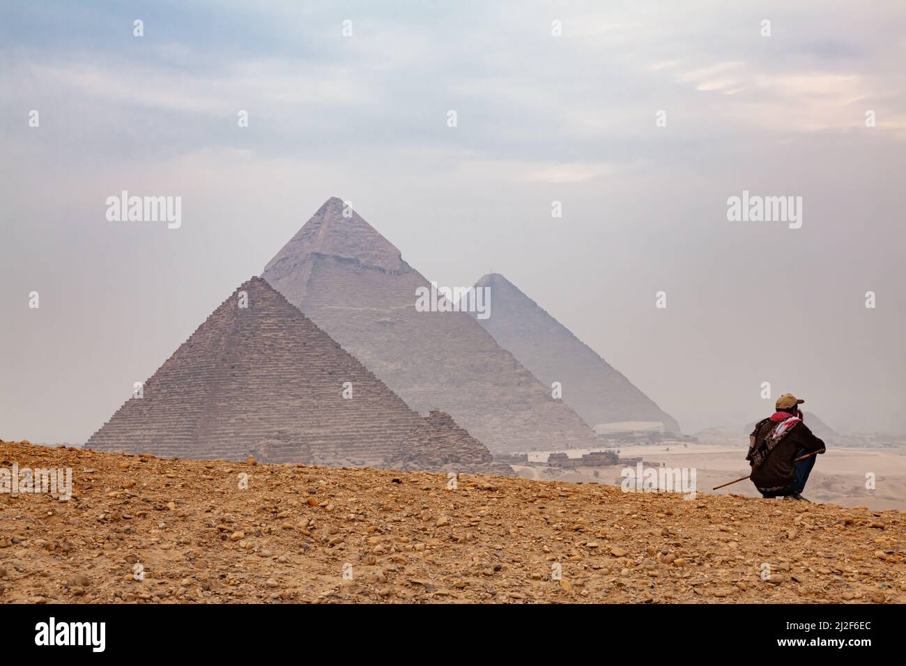 Cairo, Egitto - 30 dicembre 2011 : uomo egiziano seduto su una collina con le piramidi sfocate sullo sfondo all'altopiano di Giza in un giorno di nebbia, il Cairo, Foto Stock