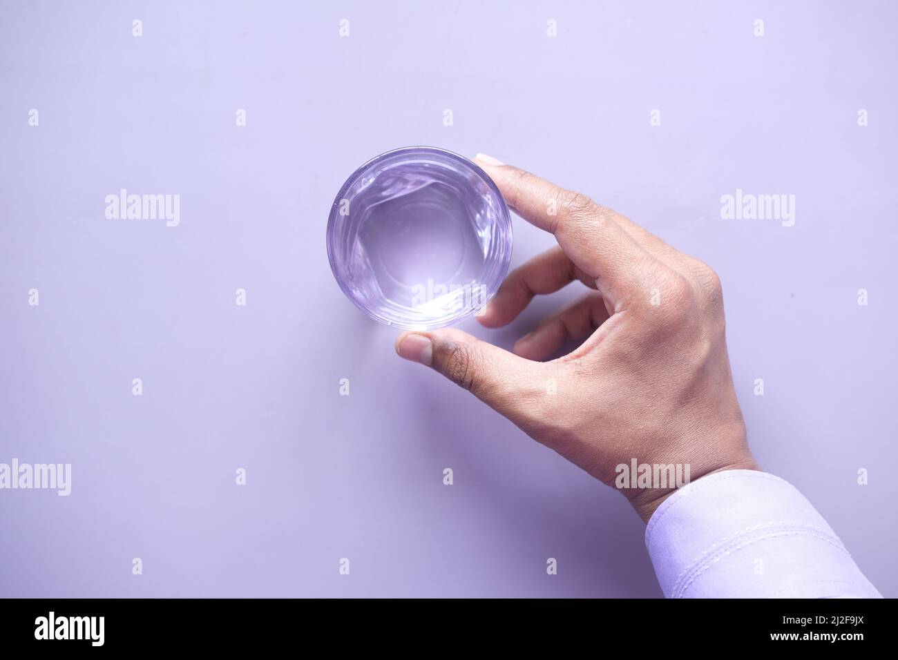 mano che tiene un bicchiere d'acqua su sfondo viola Foto Stock
