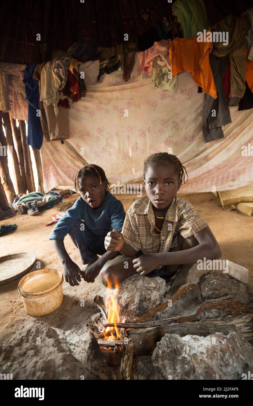 Tre bambini si scaldano al fuoco nella loro baracca di una stanza nella regione di Omusati, Namibia, Africa sudoccidentale. Foto Stock