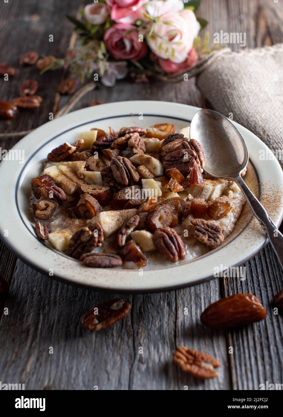 Cestino colazione con noci pecan arrostite, datteri, banane, mele e cannella su sfondo tavola di legno. Immagine verticale con spazio di copia Foto Stock