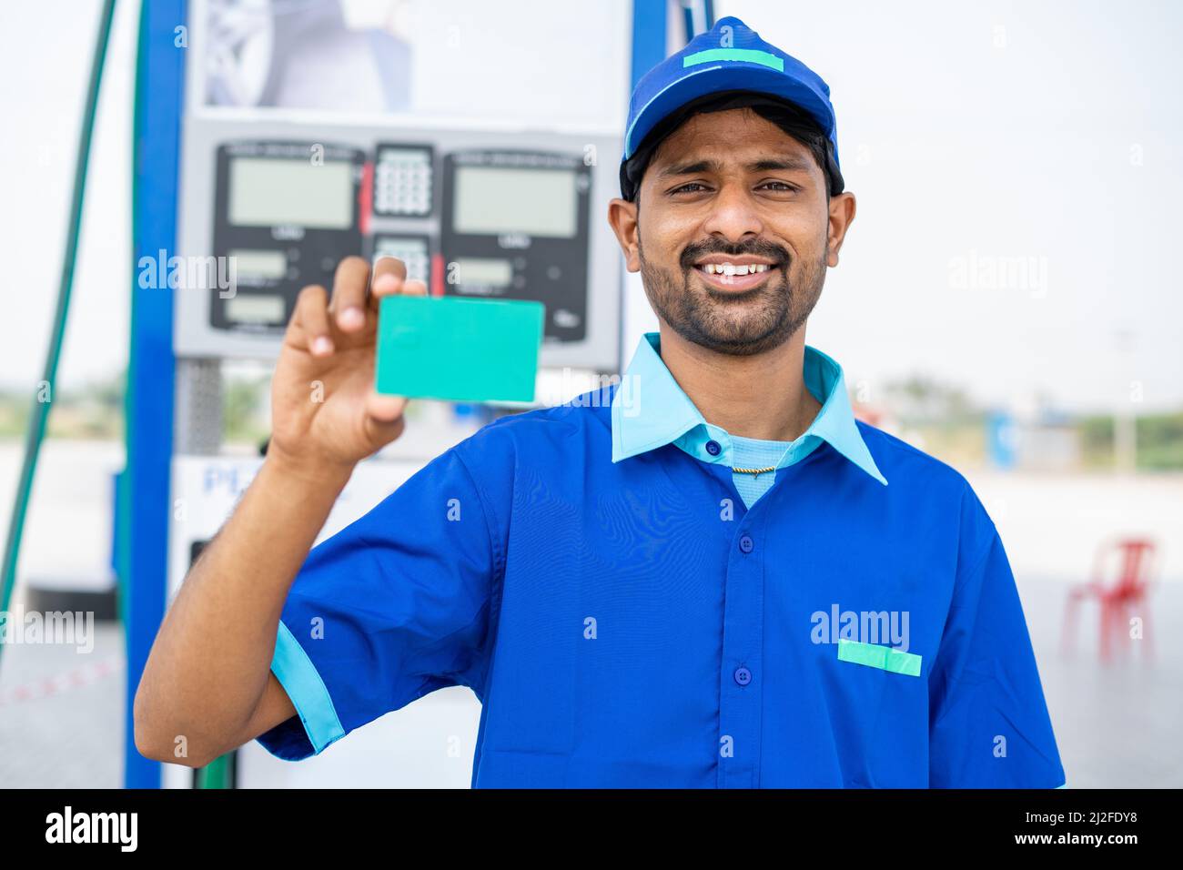 Il dipendente sorridente della pompa a benzina mostra una carta vuota con schermo verde guardando la telecamera alla stazione di rifornimento - concetto di carta d'identità del dipendente, promozione dell'annuncio e lavoro Foto Stock