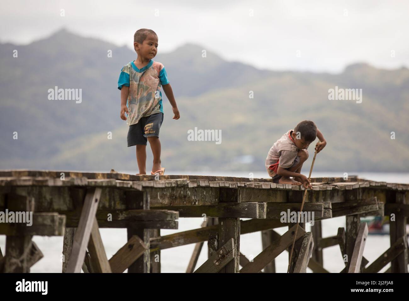 Un ragazzo cammina lungo un molo di pesca, mentre gli altri pesci con una piccola canna di legno sull'isola di Karampuang, Sulawesi occidentale, Indonesia, Asia. Foto Stock