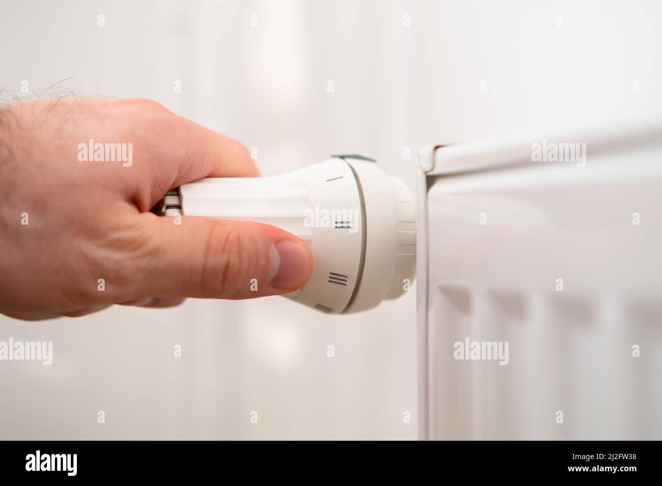 Man Hand regola la manopola di regolazione della temperatura del radiatore di riscaldamento per ridurre i costi di riscaldamento. Foto Stock