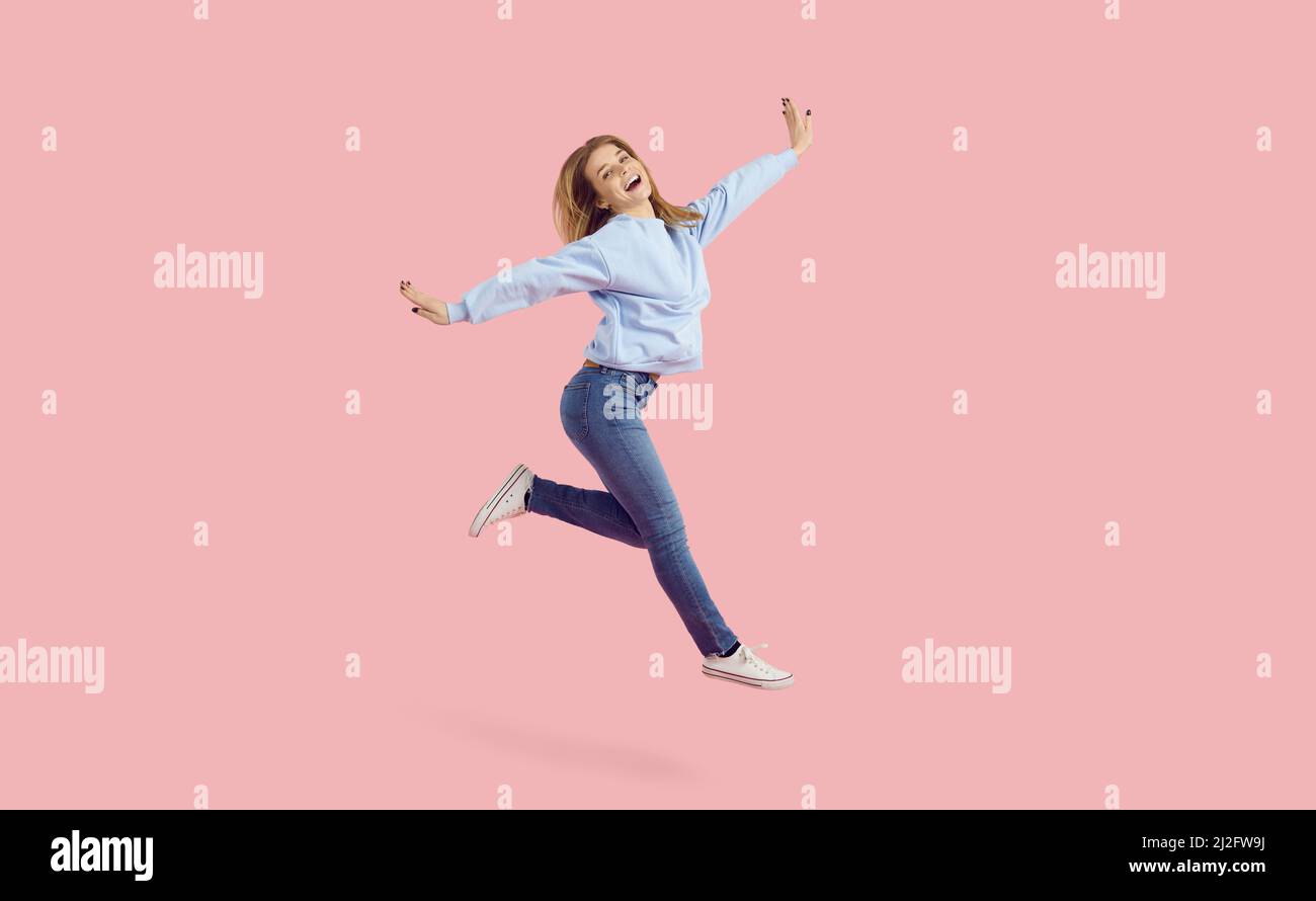 Ragazza allegra ballerina in felpa e jeans che saltano isolato su sfondo rosa Foto Stock