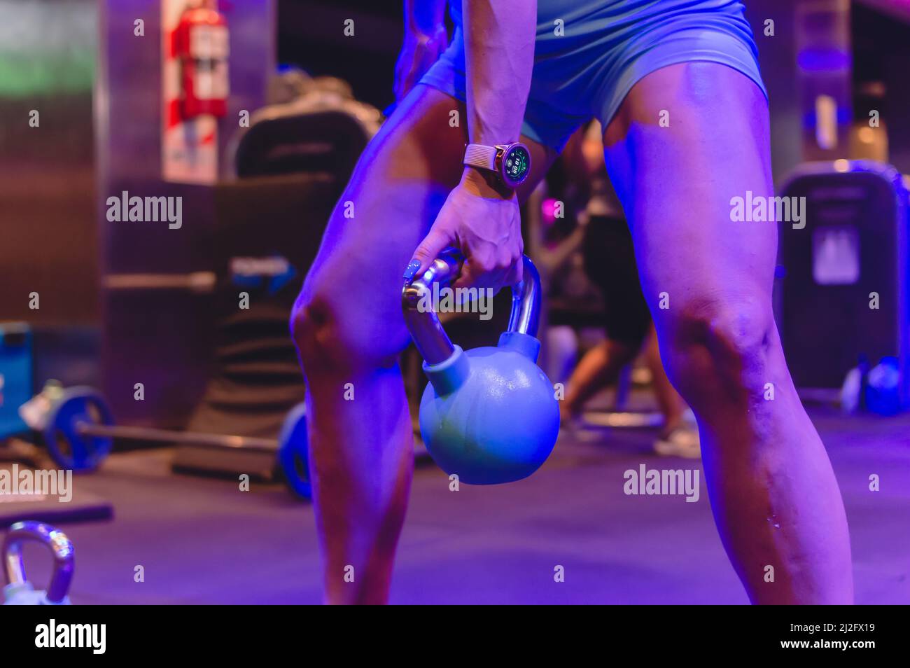 closeup irriconoscibile donna caucasica con le gambe sparse tenendo dalla vita giù un kettlebell con una mano, fitness concetto. Foto Stock