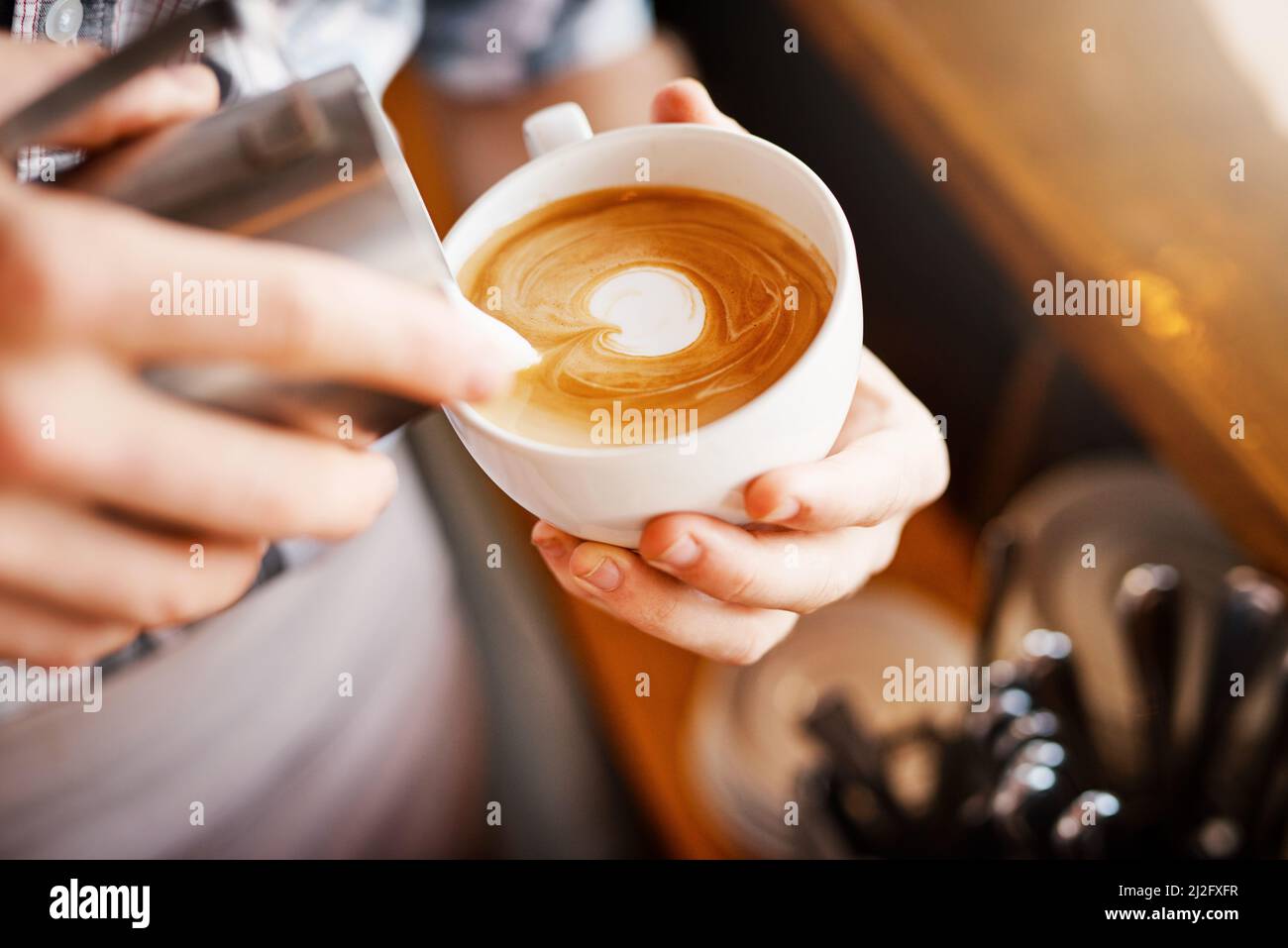 Creazione di immagini. Un'immagine ritagliata di un barista irriconoscibile che versa il latte schiumoso in una tazza di caffè caldo trasformandolo in un'immagine. Foto Stock