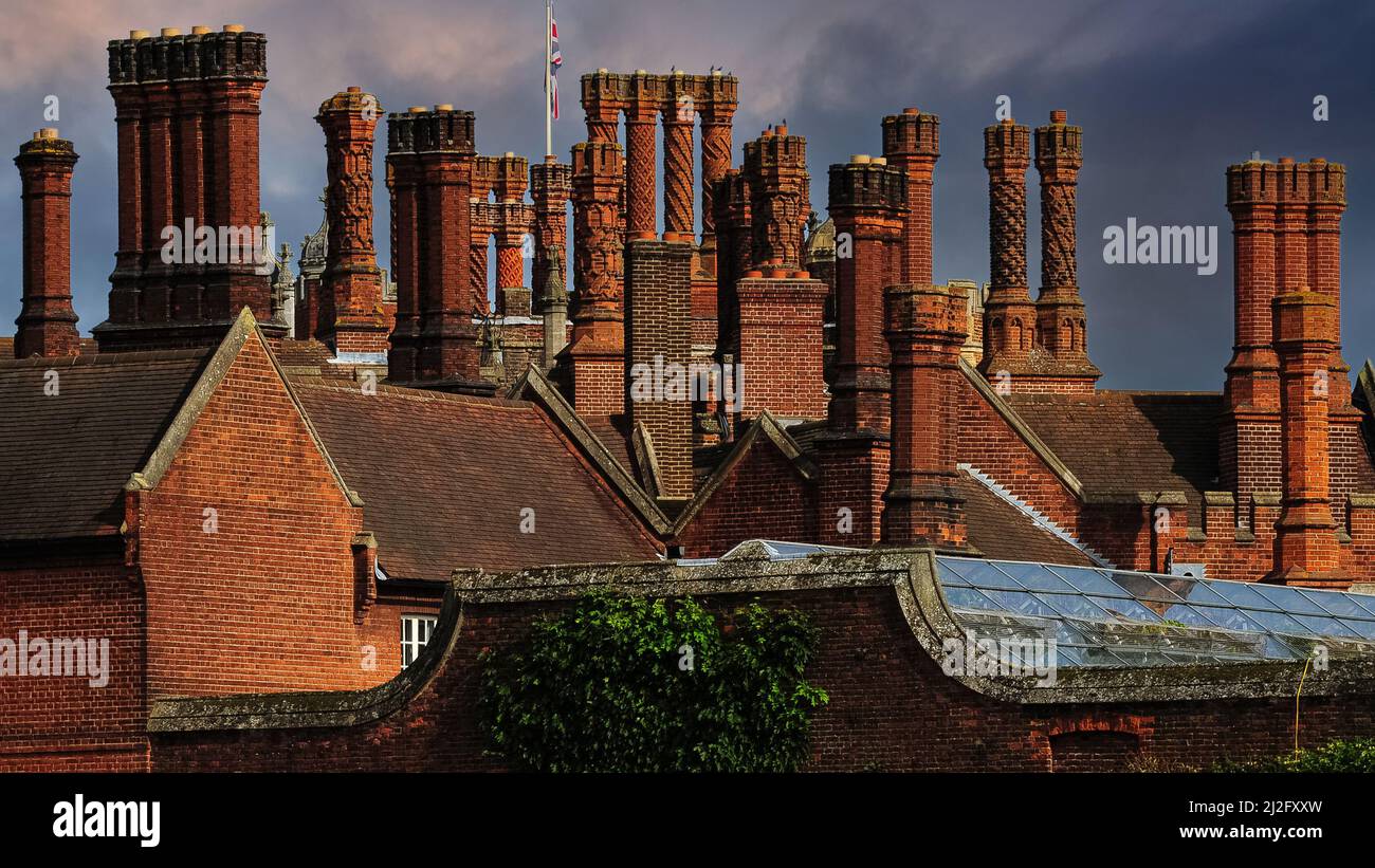 Elaborati camini in mattoni rossi in stile Tudor - non sono simili - visti contro cieli tempestosi sopra Hampton Court Palace nel borgo londinese di Richmond-upon-Thames, Inghilterra. Il palazzo, costruito nel 1515 dal cardinale Thomas Wolsey, vanta la più grande collezione di camini d'Inghilterra - 241 in tutto. Dopo che Wolsey cadde in disgrazia nel 1529, le enormi stanze di stato e appartamenti di Hampton Court furono occupati da re Enrico VIII e da più di 1.000 cortigiani. Foto Stock