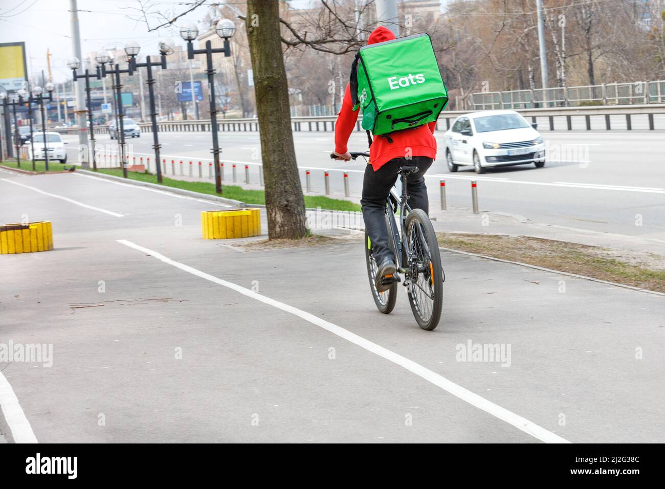 Corriere con uno zaino verde isotermico sulla schiena su una bici per la consegna di cibo in una strada della città. Foto Stock