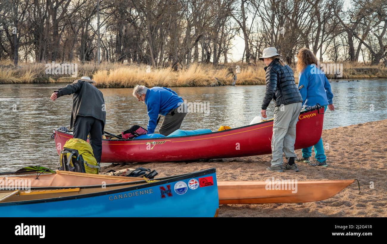 Evans, CO, USA - 26 marzo 2022: I pagaioli maschili e femminili stanno trasportando una canoa da lanciare per la prima gita primaverile in pagaiata sul fiume di South Platte in Foto Stock