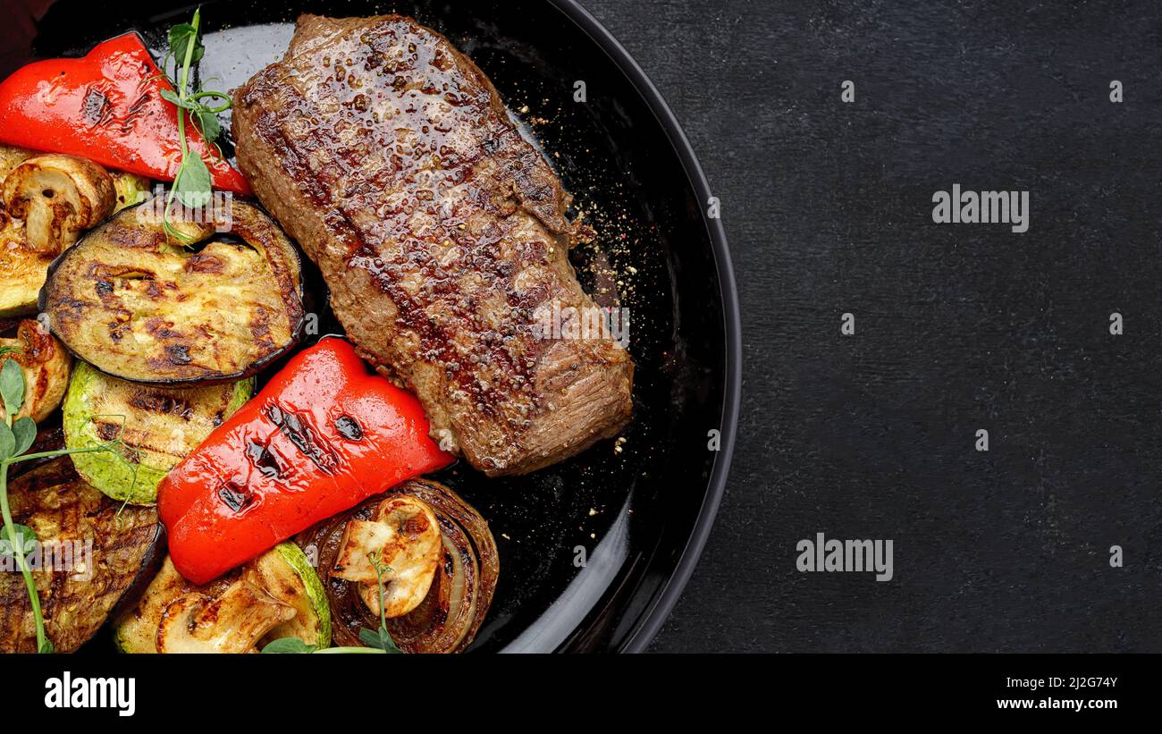 Bistecca succosa e verdure grigliate, con spezie su un piatto, su sfondo scuro Foto Stock