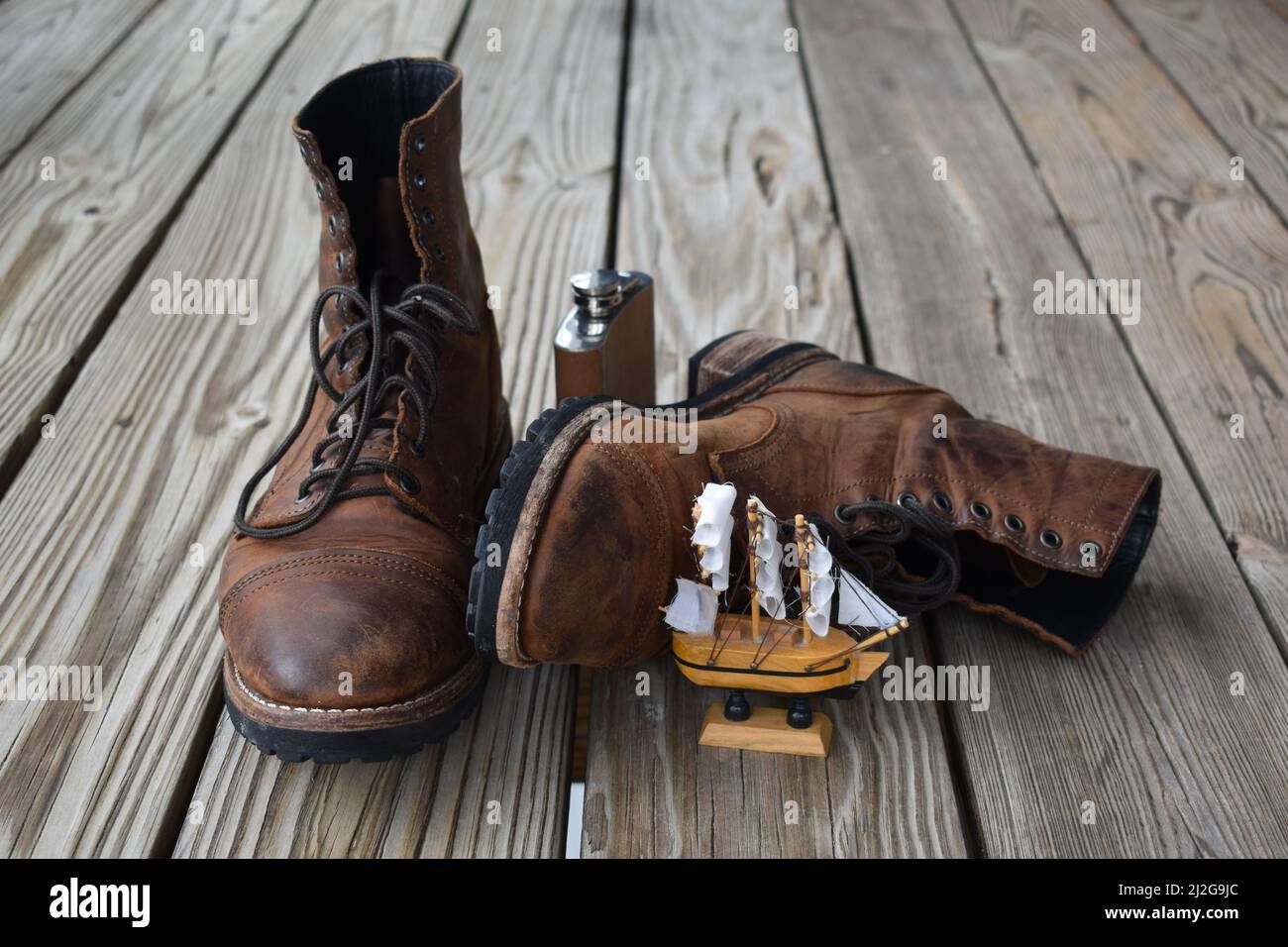 Vecchi stivali in pelle marrone, fiasca marrone chiaro e piccola barca a  vela su superficie di legno isolato Foto stock - Alamy