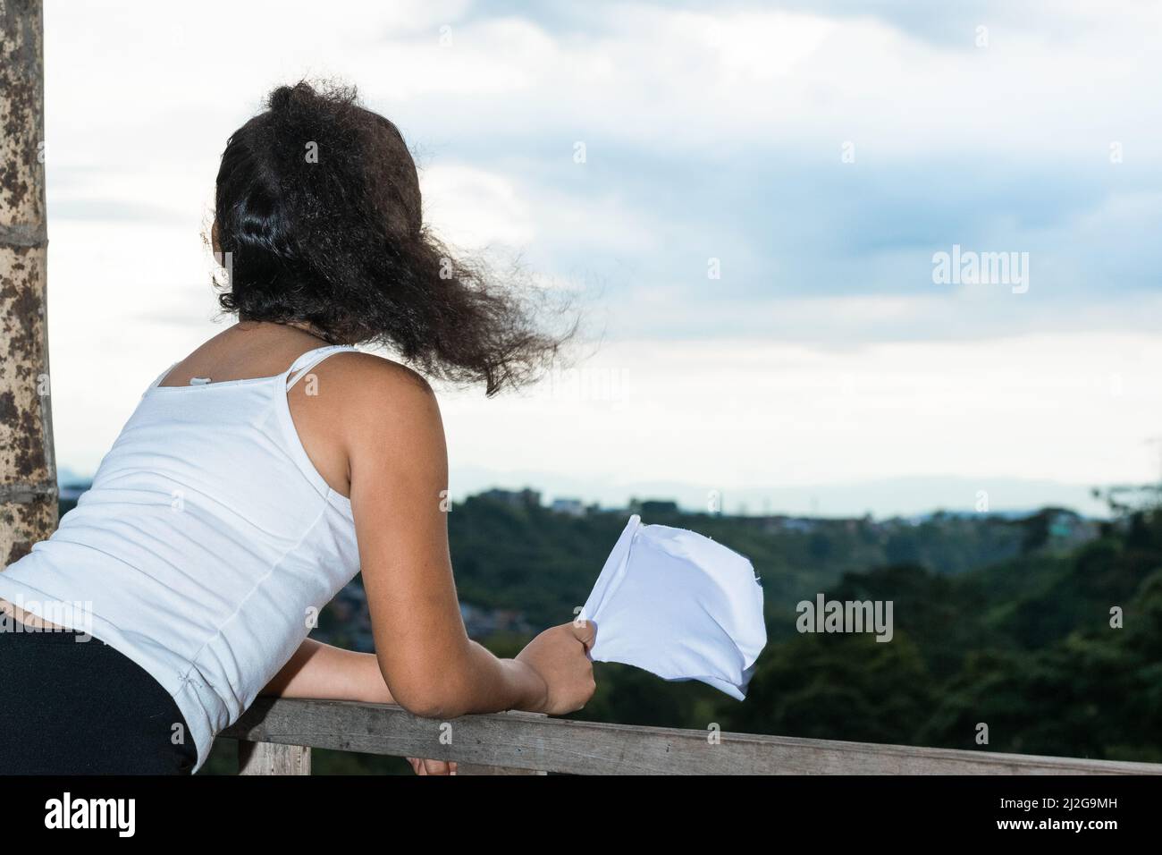 scatto della parte posteriore di una ragazza latina, brunette guardando verso l'orizzonte mentre sventola la sua bandiera bianca (bandiera di pace). colombiana ragazza che desidera la pace nel suo c Foto Stock