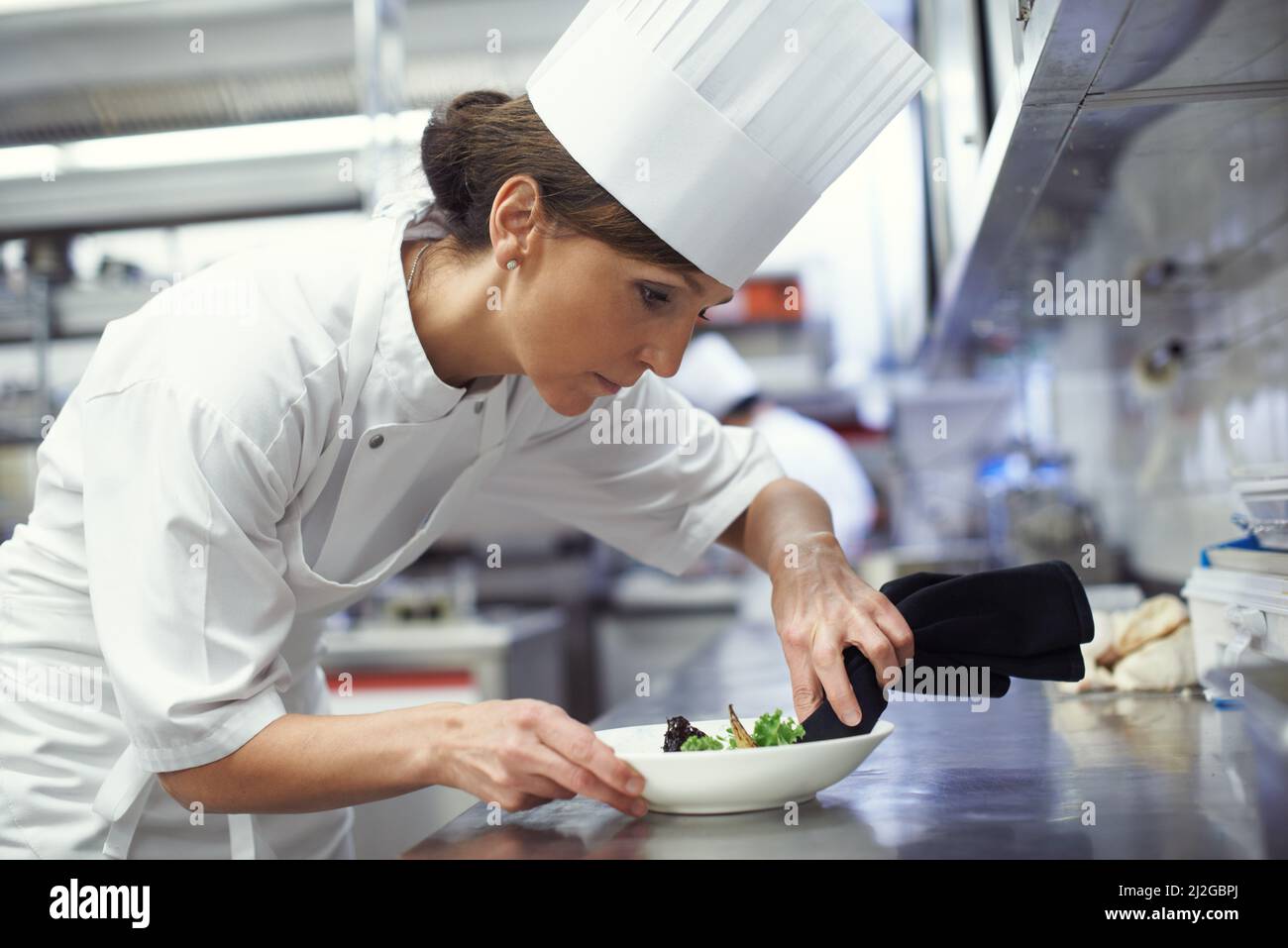 Chef al lavoro. Shot di uno chef che mette i tocchi finali su un piatto da pranzo in una cucina professionale. Foto Stock