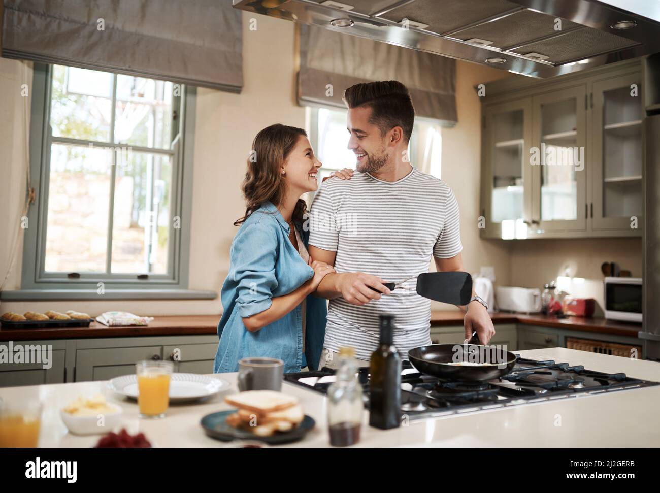 Stai cercando di segnare alcuni punti brownie. Shot di una giovane donna che abbraccia il suo partner mentre cuoca la colazione. Foto Stock