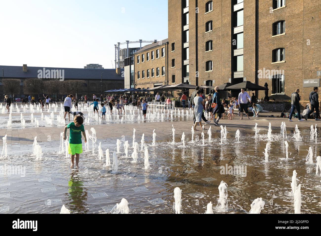 I bambini giocano al sole primaverile nelle fontane di Granary Square, a Kings Cross, a nord di Londra, Regno Unito Foto Stock