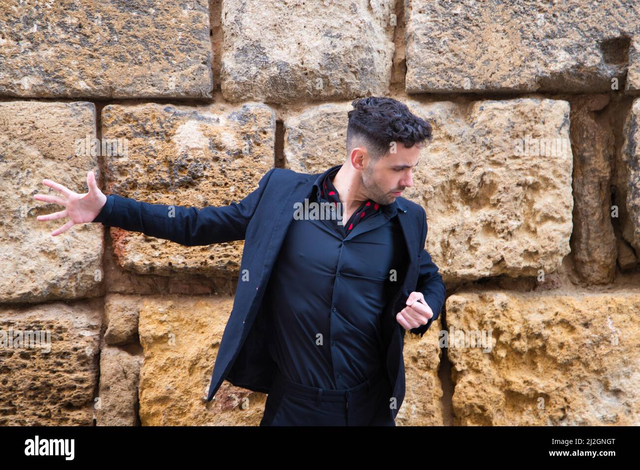 Un uomo zingaro che balla flamenco, indossando abiti neri e scarpe rosse, su uno sfondo di pietra muro, Spagna Foto Stock