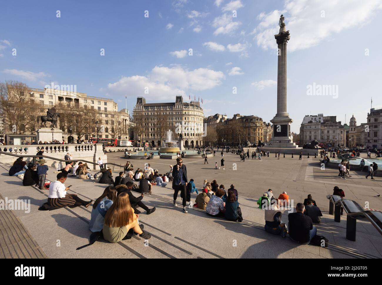 Nelsons colonna Trafalgar Square Londra scena - persone che godono il sole di primavera seduta fuori nel centro di Londra WC2, Londra UK Foto Stock