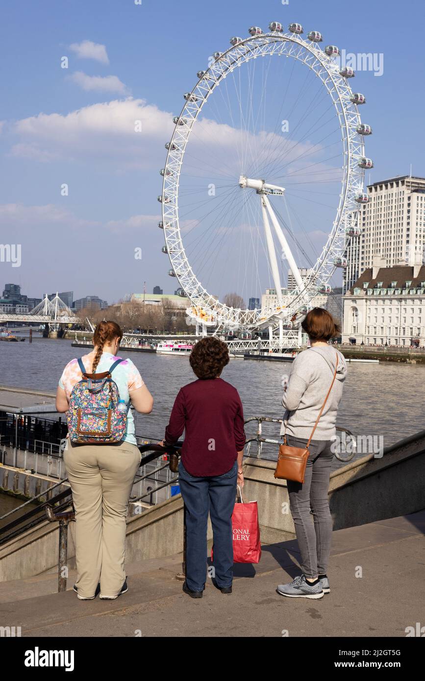 Turismo di Londra; tre turisti che guardano il London Eye, noto anche come Millennium Wheel, in una giornata fuori, da Westminster Bridge, Londra UK Foto Stock