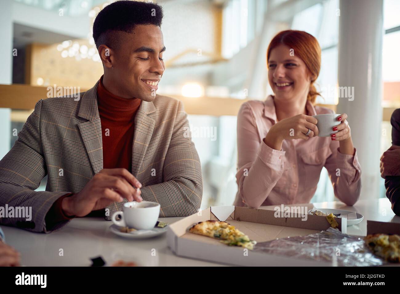 Un giovane uomo d'affari sta chiacchierando con una collega mentre si godono il caffè dopo un pranzo in un'atmosfera piacevole nel gruppo di costruzione dell'azienda Foto Stock