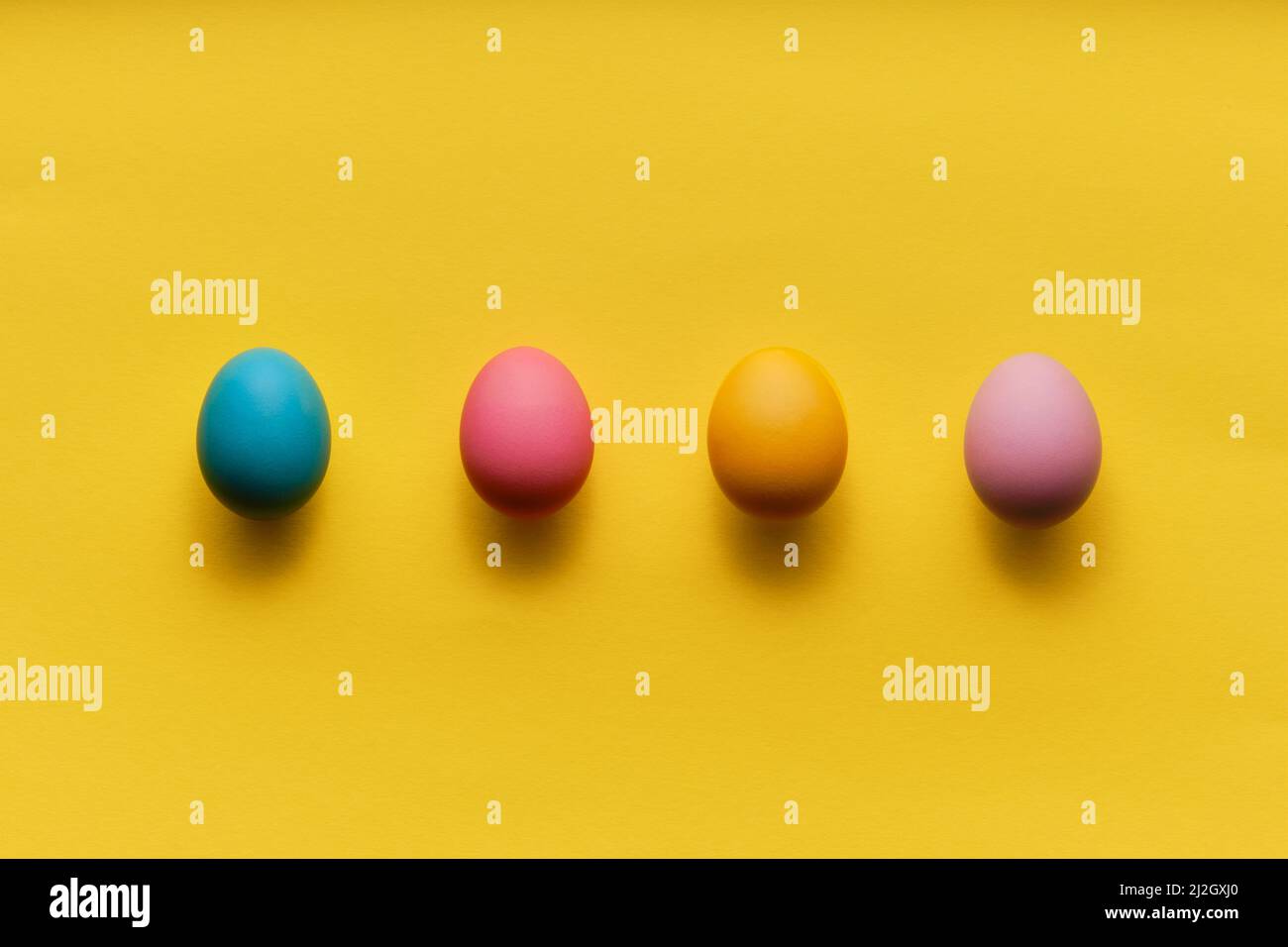 quattro uova di pasqua colorate in fila su carta gialla con abbondanza di spazio per la copia Foto Stock