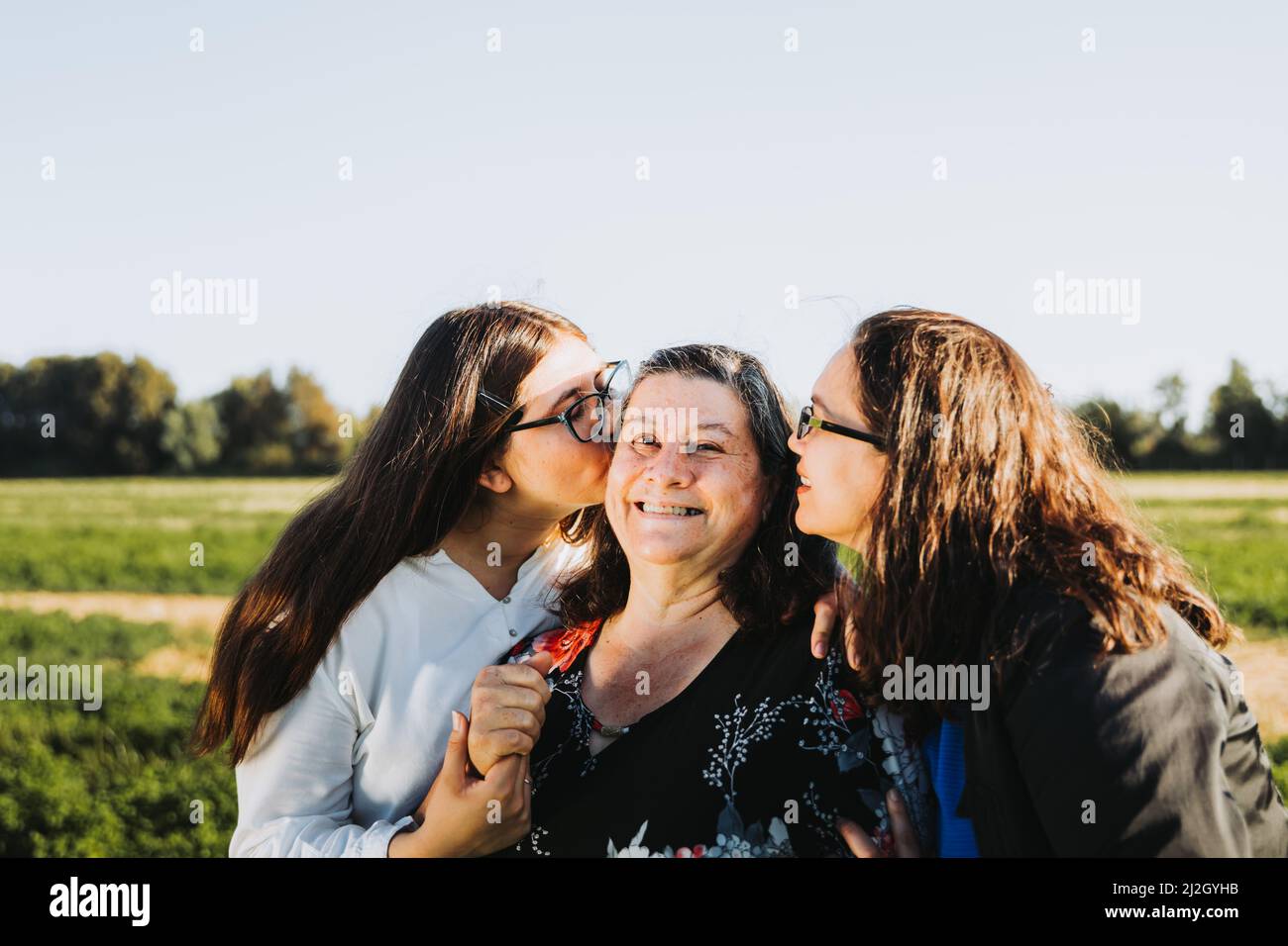 Famiglia femminile sorridente e baciata sul campo in un pomeriggio di sole. Giornata delle madri. Foto Stock