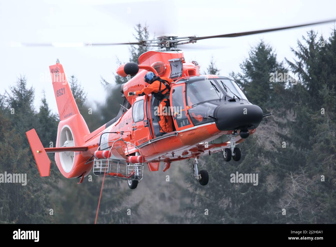 Un membro dell'equipaggio a bordo di un elicottero MH-65 Dolphin osserva i membri dell'equipaggio della piccola barca sotto l'elicottero durante l'addestramento del paranco nel fiume Umpqua, vicino a Winchester Bay, Oregon, 14 marzo 2022. Le operazioni di addestramento sono tenute regolarmente per assicurare che le capacità di ricerca e di salvataggio degli equipaggi della Guardia Costiera rimani all'alto livello previsto da loro. Foto Stock