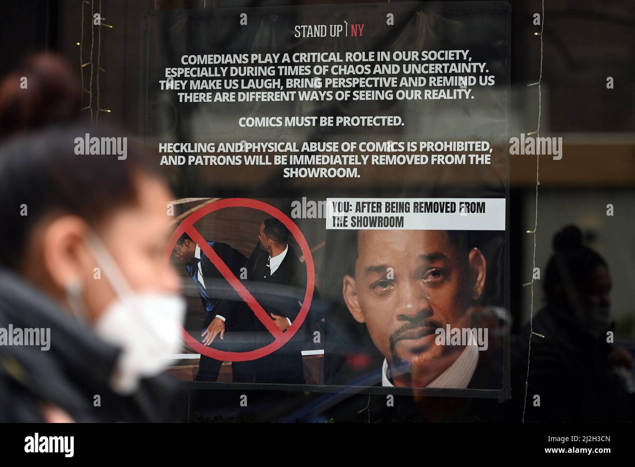 New York, Stati Uniti. 01st Apr 2022. Una donna che indossa una maschera cammina accanto a un poster impostato nella finestra del New York Comedy Club Stand Up NY, avverte i patroni che qualsiasi heckling o violenza fisica contro comics performance non sarà tollerato, New York, NY, 1 aprile 2022. L'avvertimento è in reazione all'attore Will Smith che schiaffa il comico Chris Rock durante gli Academy Awards del 94th il 27 marzo, reagendo allo scherzo presentato da MR. Rock per quanto riguarda la testa rasata della moglie di MR. Smith, che soffre di alopecia. (Foto di Anthony Behar/Sipa USA) Credit: Sipa USA/Alamy Live News Foto Stock