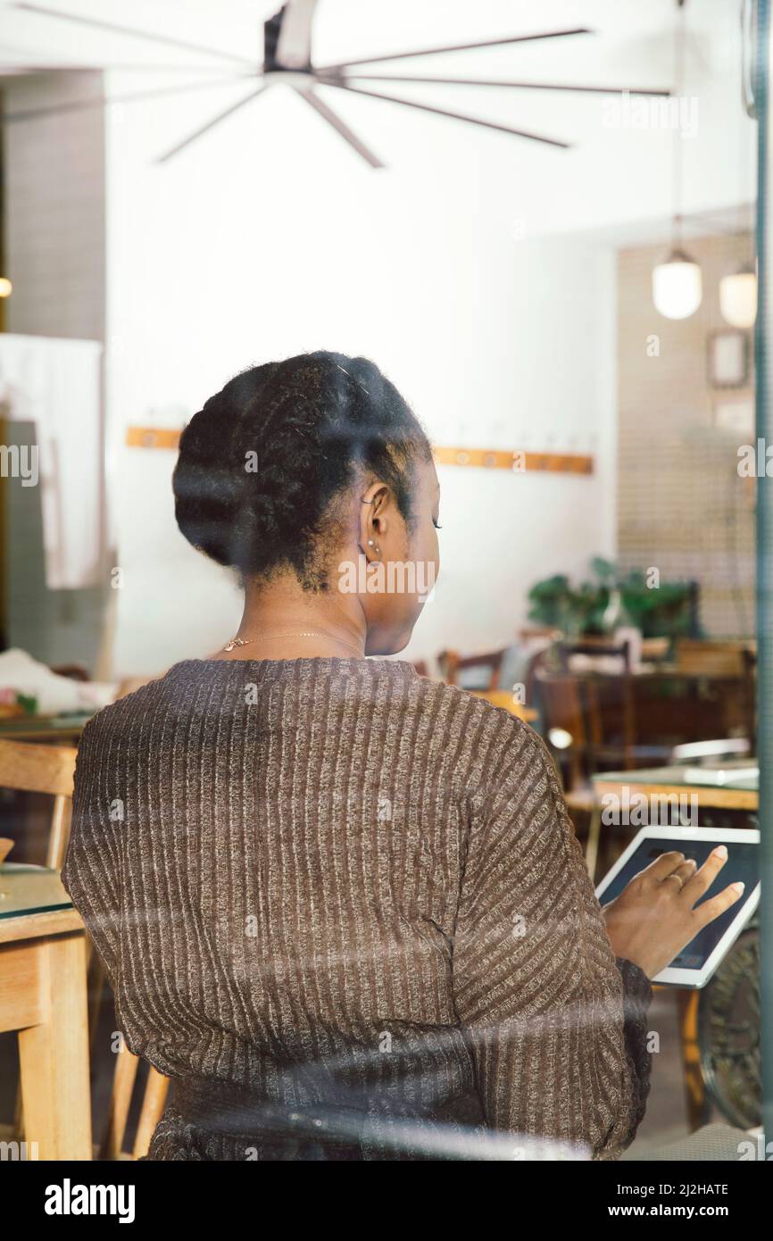 Vista posteriore di una donna che utilizza un tablet digitale in un bar Foto Stock