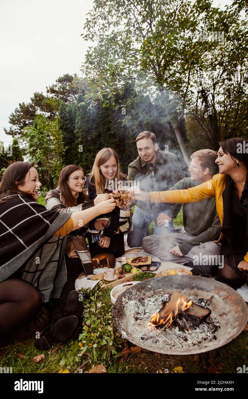 Gruppo di amici che tostano intorno alla fossa del fuoco in giardino Foto Stock