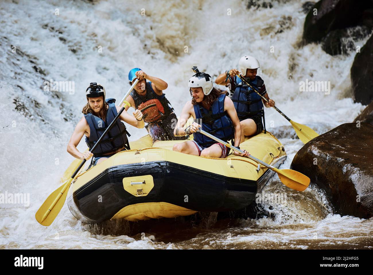 Siamo un motore umano. Sparato di un gruppo di giovani uomini determinati su una barca di gomma occupato a pedalare su forti rapide del fiume all'esterno durante il giorno. Foto Stock