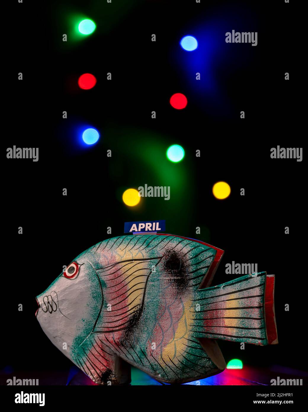 Un divertente pesce sciocco di legno aprile con luci colorate rotonde sullo sfondo Foto Stock