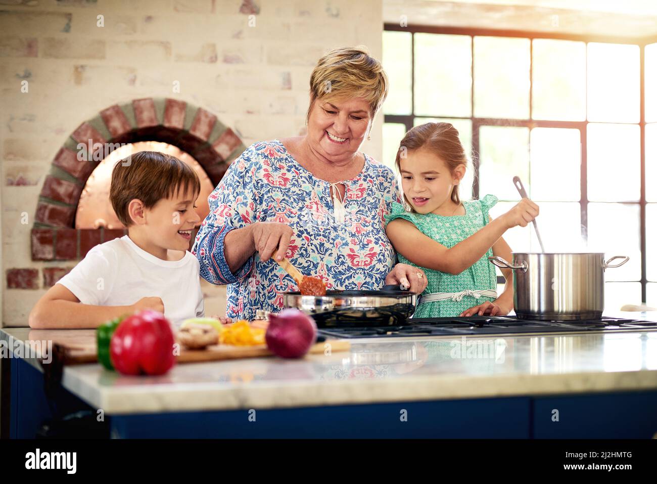 La nonna è così fortunata da avere due piccoli aiutanti desiderosi. Shot di una nonna che cucinava con i suoi due nipoti a casa. Foto Stock