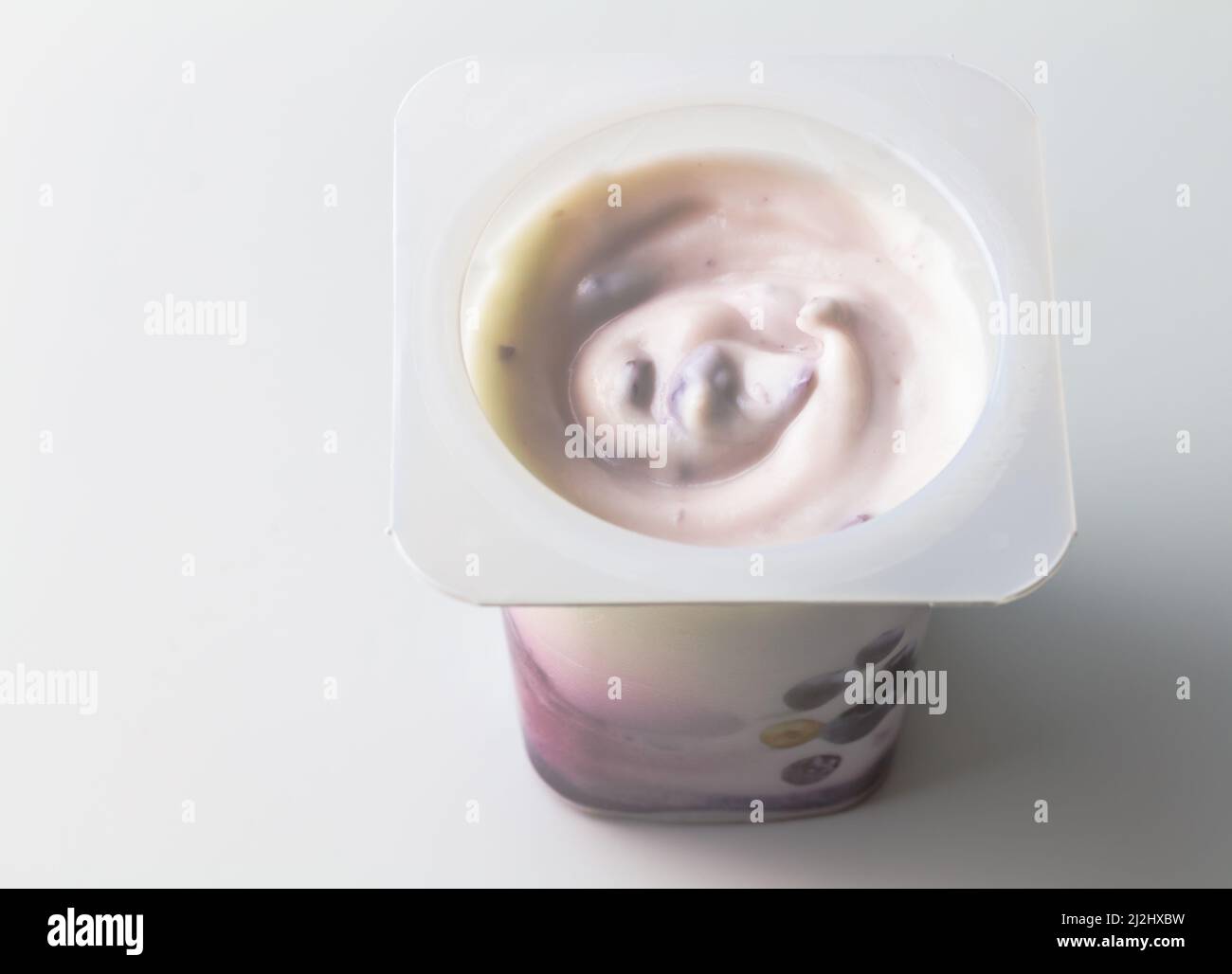 Vista dall'alto del contenitore di plastica con gustoso dessert o crema di yogurt bianco e mirtillo isolato su sfondo bianco Foto Stock