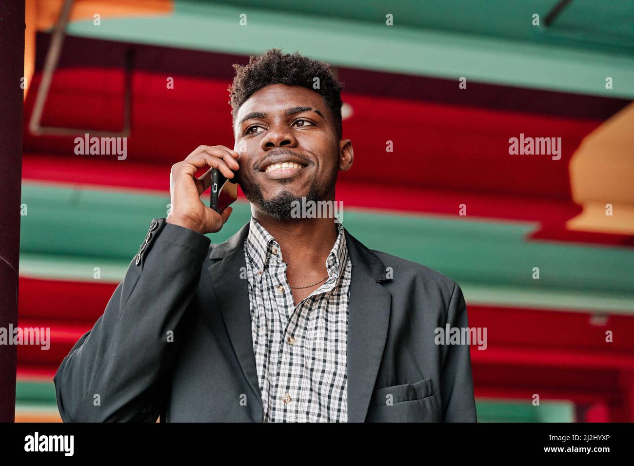 Ritratto di un felice uomo afroamericano che parla su uno smartphone con un colorato sfondo cittadino Foto Stock