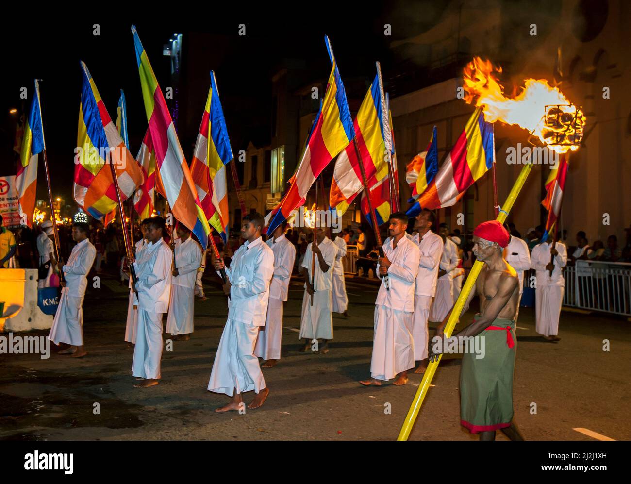 I portatori di bandiera buddista e un portatore di torcia sfilano lungo una strada a Kandy in Sri Lanka durante l'Esala Perahera (grande processione). Foto Stock