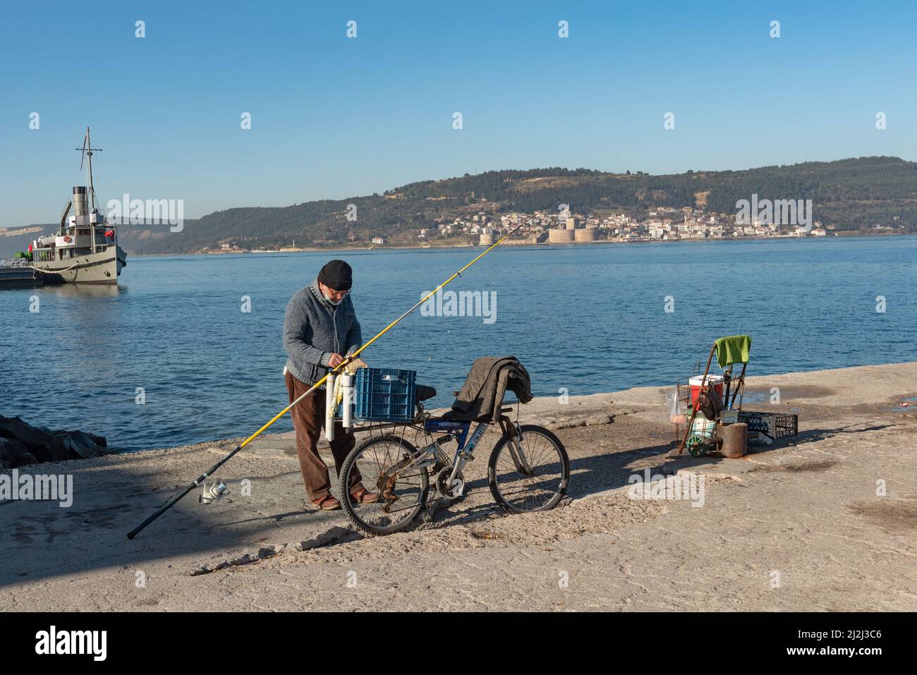 Canakkale, Turchia. Febbraio 18th 2022 Un pescatore turco sul molo di Canakkale, con i Dardanelli dritto, la penisola di Gallipoli e Kilibaher Foto Stock