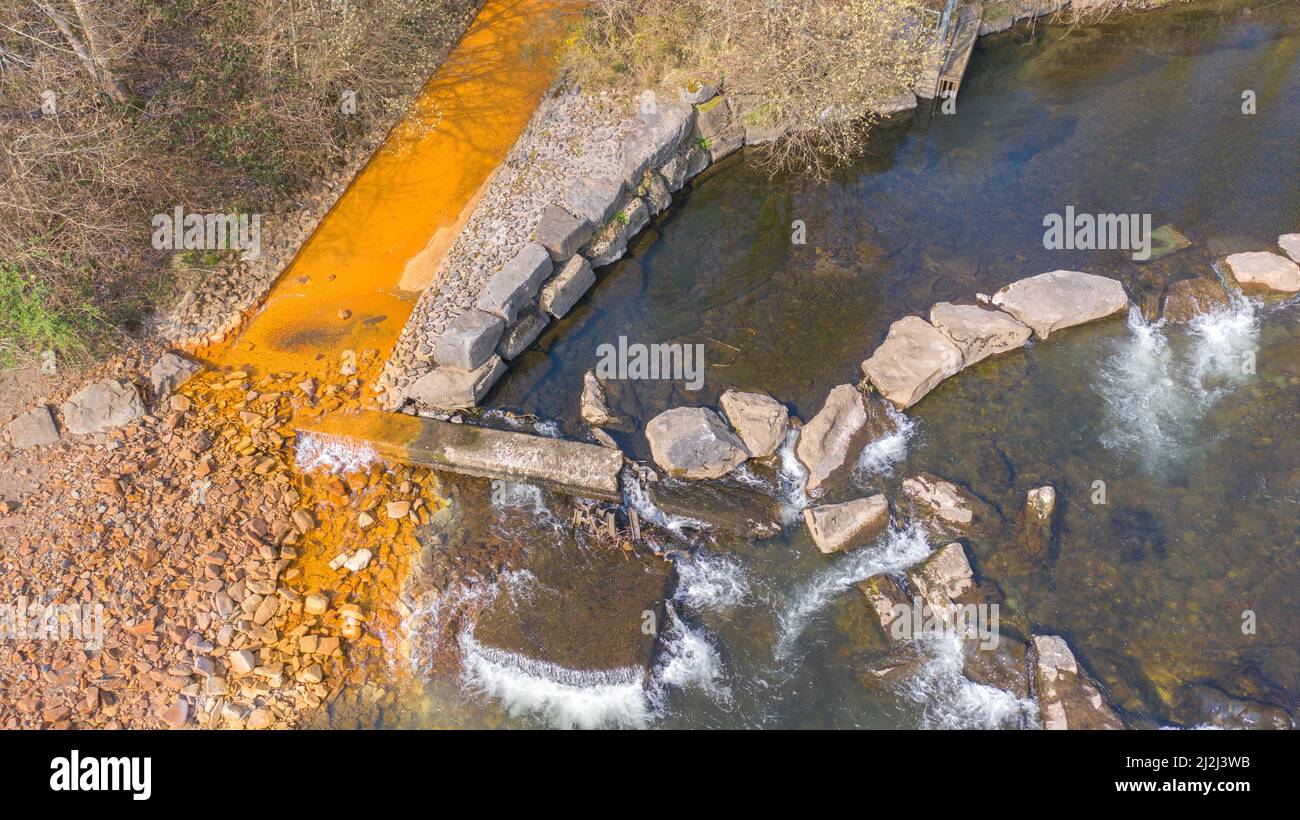 Vista aerea della colorazione arancione ossido di ferro in corrente che entra nel fiume Neath ad Abergarwed. La fonte è lo scarico di acqua da una miniera di carbone abbandonata. Foto Stock