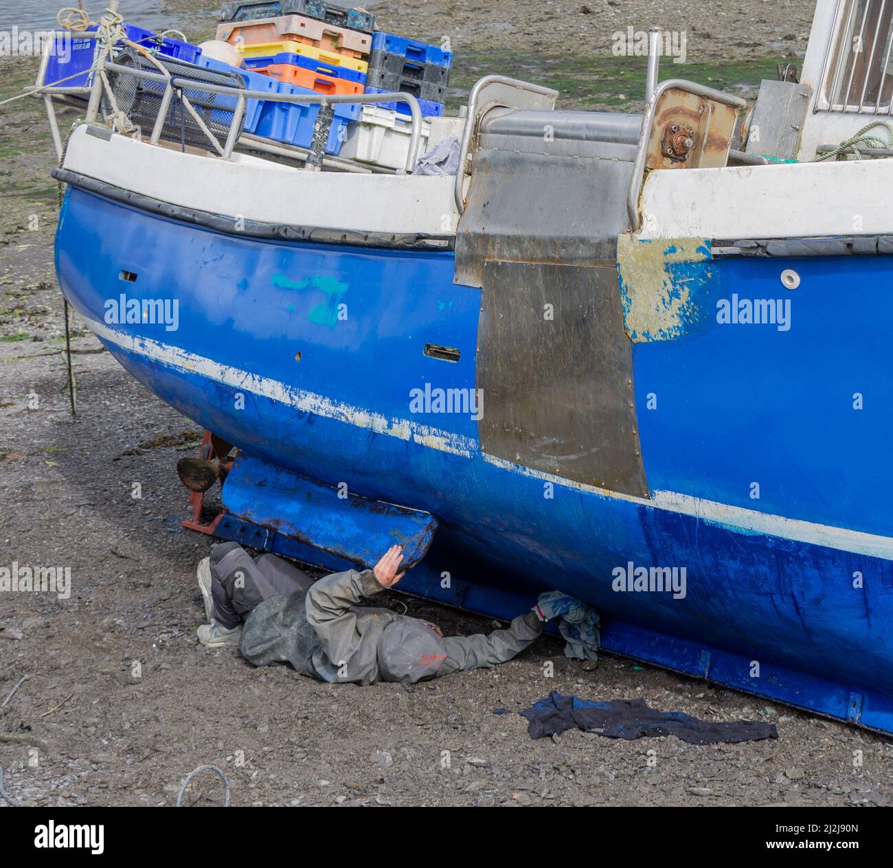 Uomo sdraiato sulla schiena a bassa marea pulizia scafo in vetroresina Foto Stock
